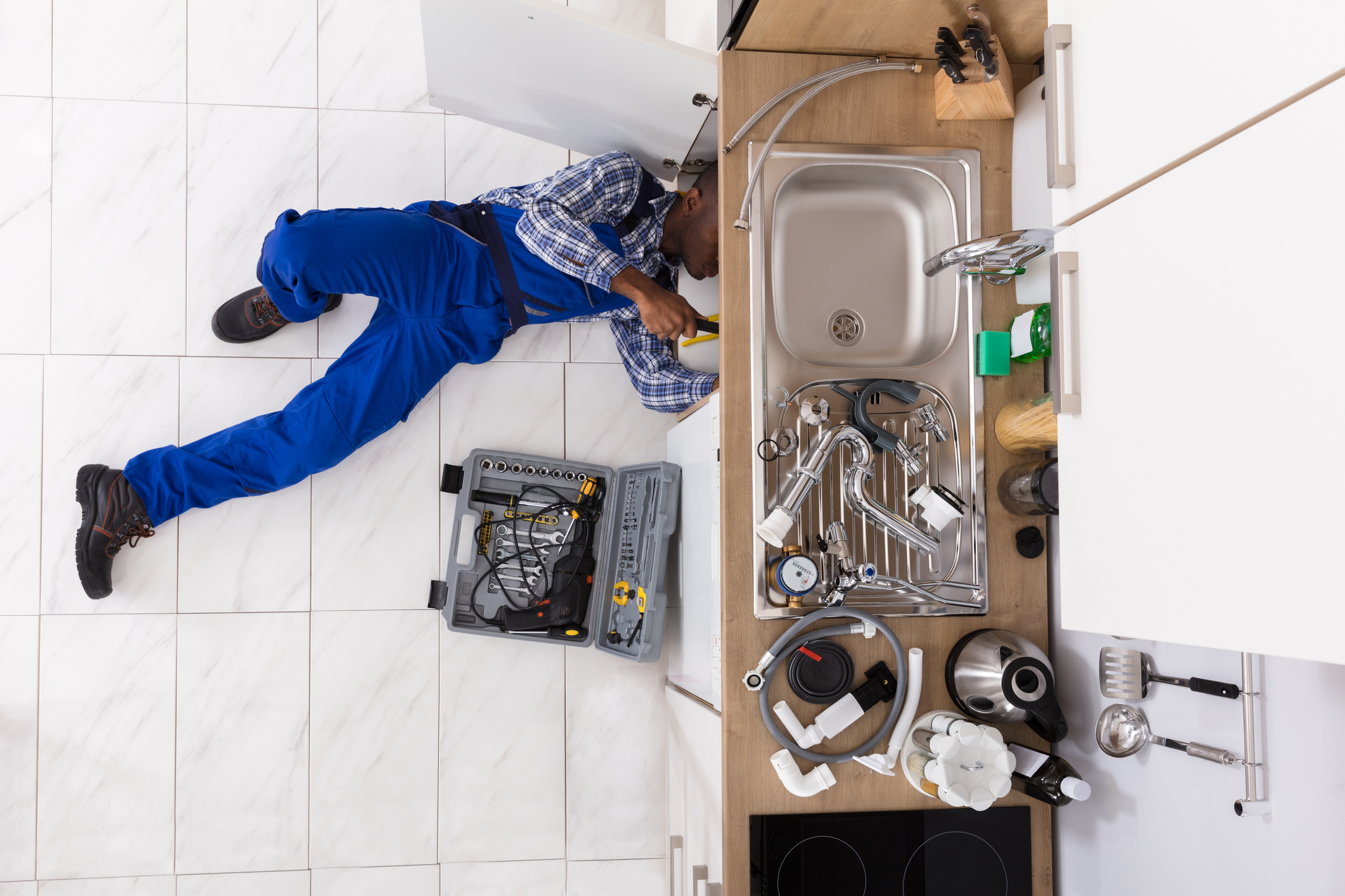 High Angle View Of Handyman Lying On Floor Repairing Sink In Kitchen With Toolbox